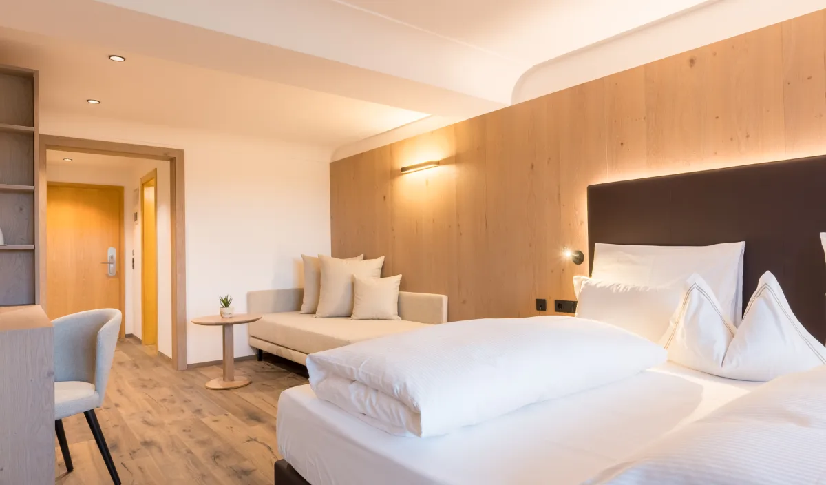 Doppelbett mit gepolstertem Kopfteil, Holzwandverkleidung und Tagesbett mit Kissen im Zimmer Panorama Superior.