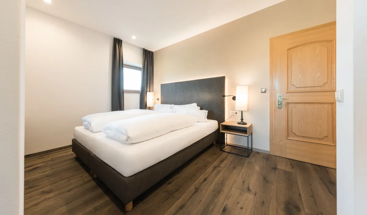 Camera da letto con letto matrimoniale, comodino, lampada da lettura e porta in legno nella Sun Suite.