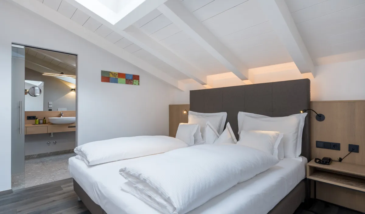 Seconda camera da letto dell'Attico Suite con letto matrimoniale, lucernario e porta del bagno aperta.