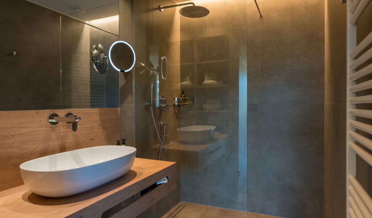 Badezimmer mit Aufsatzwaschbecken auf Holzwaschtisch, begehbarer Regendusche und Natursteinwänden.