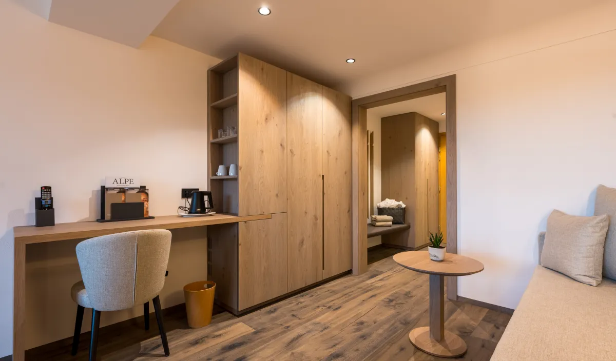 Schreibtisch mit Stuhl, Holzschrank, Kaffeemaschine und Durchgang zum Eingangsbereich mit Tagesbett.