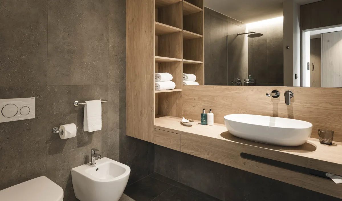 Bagno con lavabo d'appoggio su mobile in legno, bidet, mensole per asciugamani e doccia a pioggia visibile nello specchio.