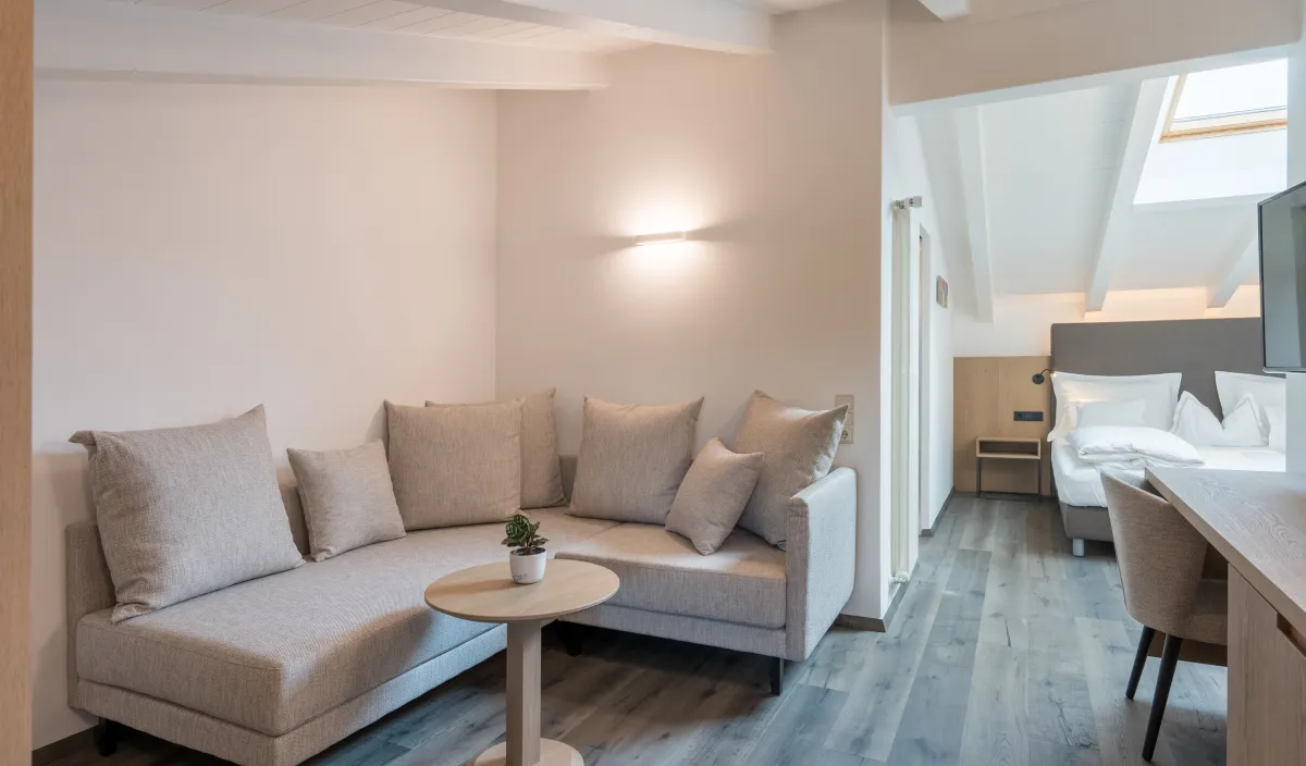 Accogliente zona giorno con divano ad angolo, tavolino e vista sulla camera da letto dell'Attico Suite.