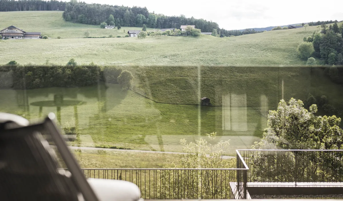 Vista dal balcone su prati verdi e dolci colline con sdraio in primo piano.
