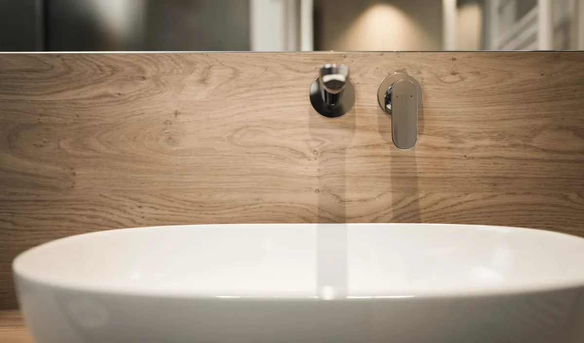Primo piano del lavabo d'appoggio con rubinetteria a parete e pannello in legno nel bagno.