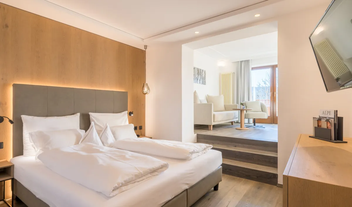Zona notte della Sun Suite con letto matrimoniale, parete in legno e gradini verso il soggiorno rialzato con poltrone.