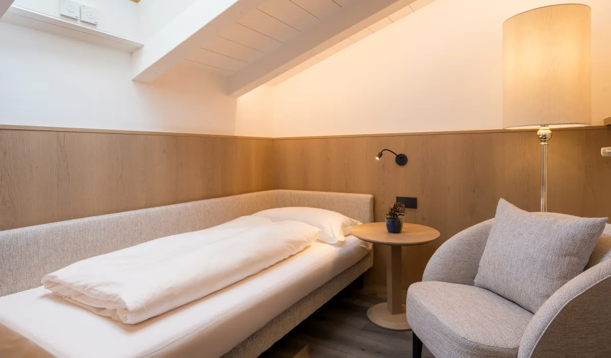 Zona notte aggiuntiva sotto il tetto spiovente con letto singolo, poltrona e lucernario.