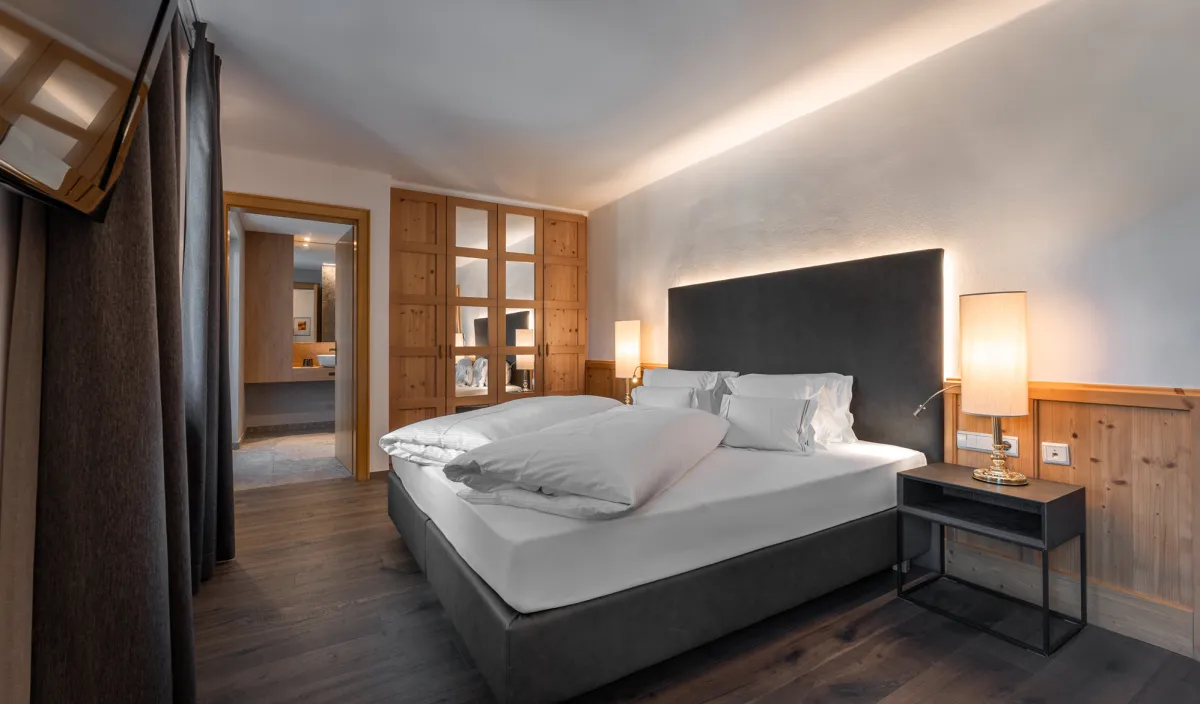 Doppelzimmer Classic mit Doppelbett, Holzschrank mit Glastüren, Nachttischleuchten und Durchgang zum Badezimmer.