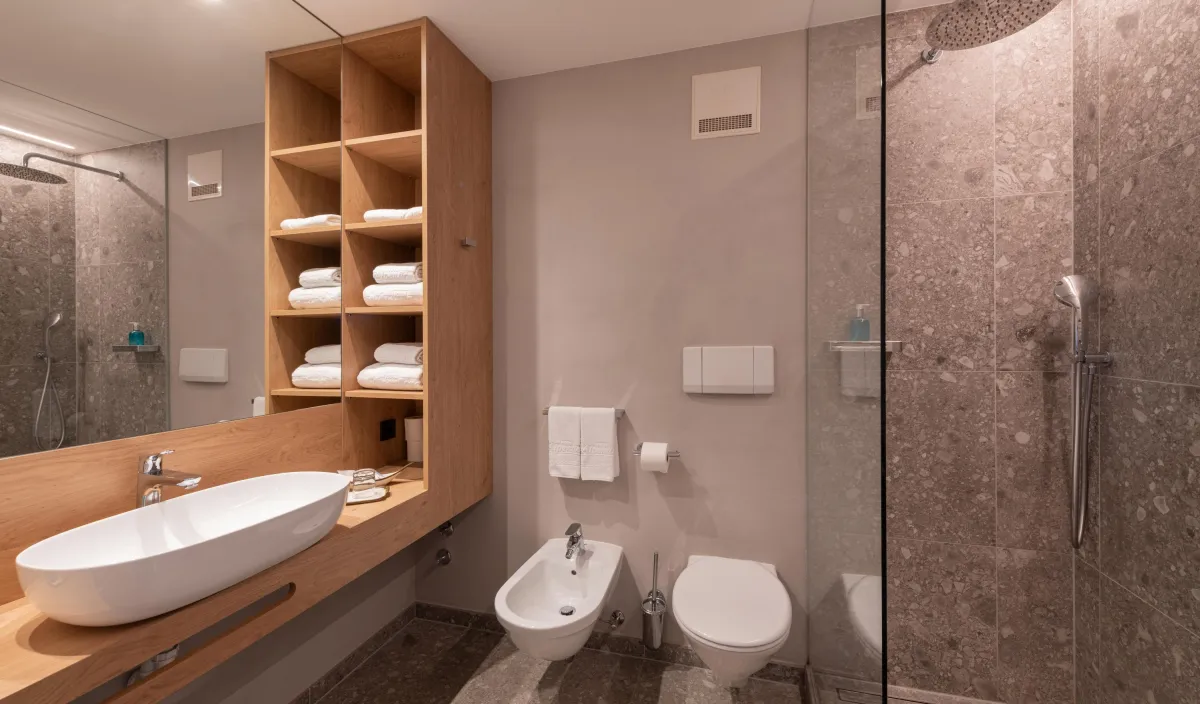 Bagno con lavabo d'appoggio su mobile in legno, mensole per asciugamani, bidet, WC e doccia a pioggia.