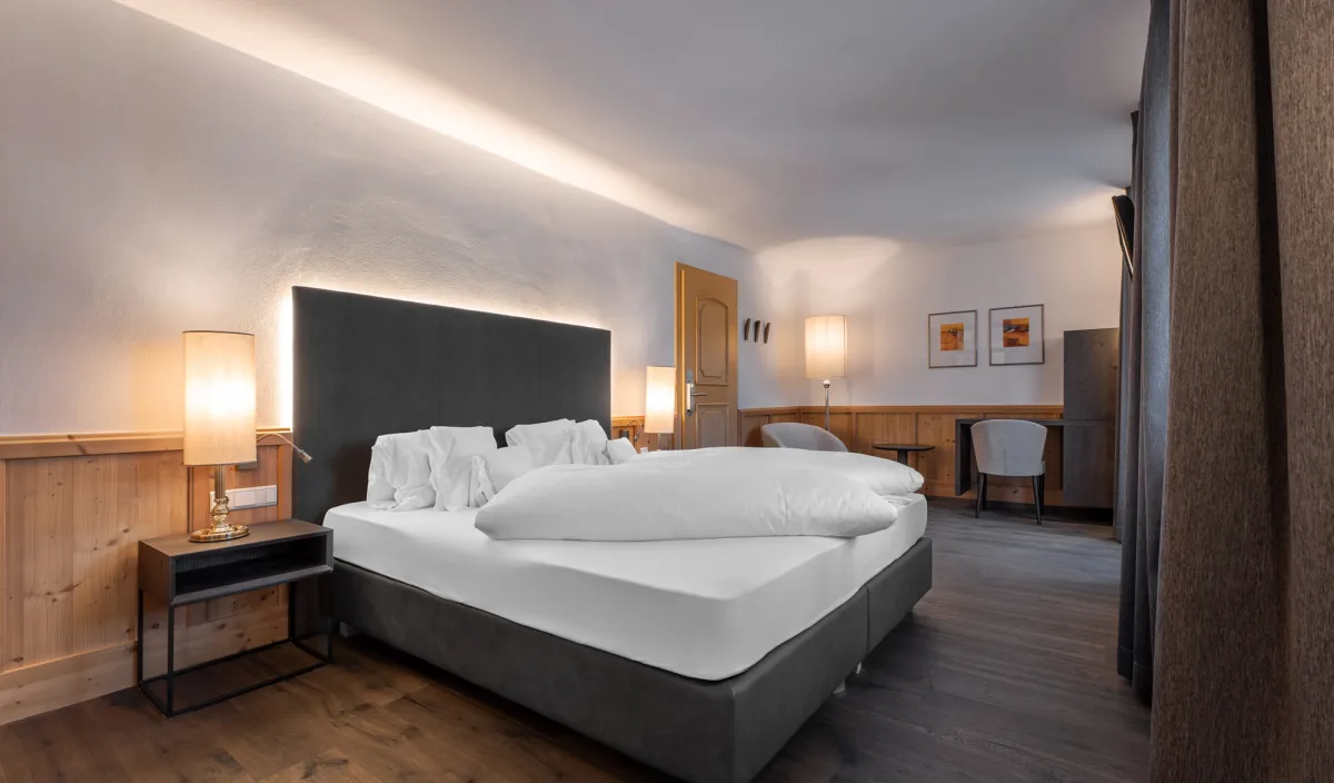 Doppelzimmer Classic mit Doppelbett, Holzvertäfelung, Nachttischleuchten, Schreibtisch und zwei Bildern an der Wand.