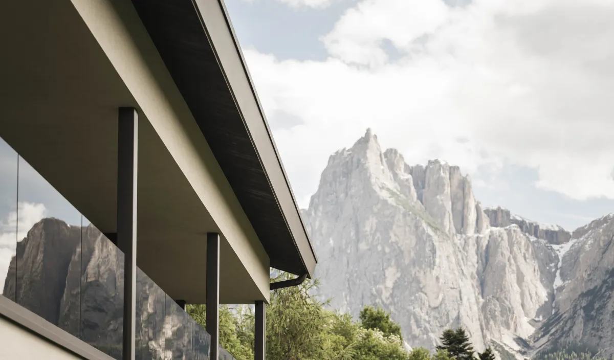 Facciata del Wellnesshotel Alpenflora con balconi in vetro e vista sulle pareti rocciose delle Dolomiti.