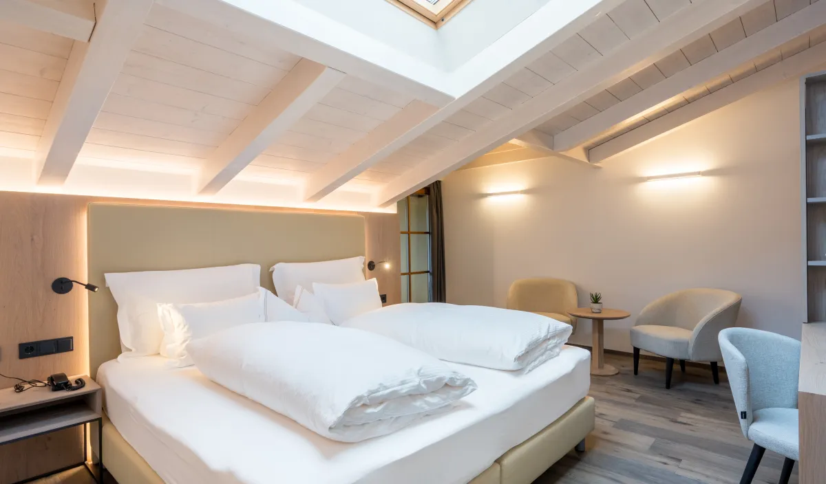 Dachgeschoss-Variante mit Doppelbett, Dachfenster, weißer Holzbalkendecke und zwei Sesseln.