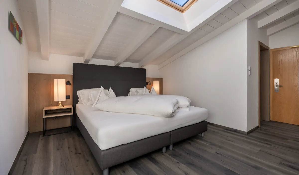 Camera da letto con letto matrimoniale, comodini e lucernario aperto con cielo azzurro nell'Attico Suite.