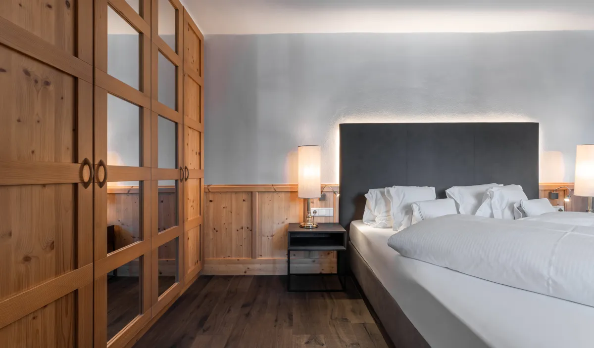Doppelbett mit anthrazitfarbenem Kopfteil, grossem Holzschrank mit Glastüren und Holzvertäfelung im Zimmer Classic.