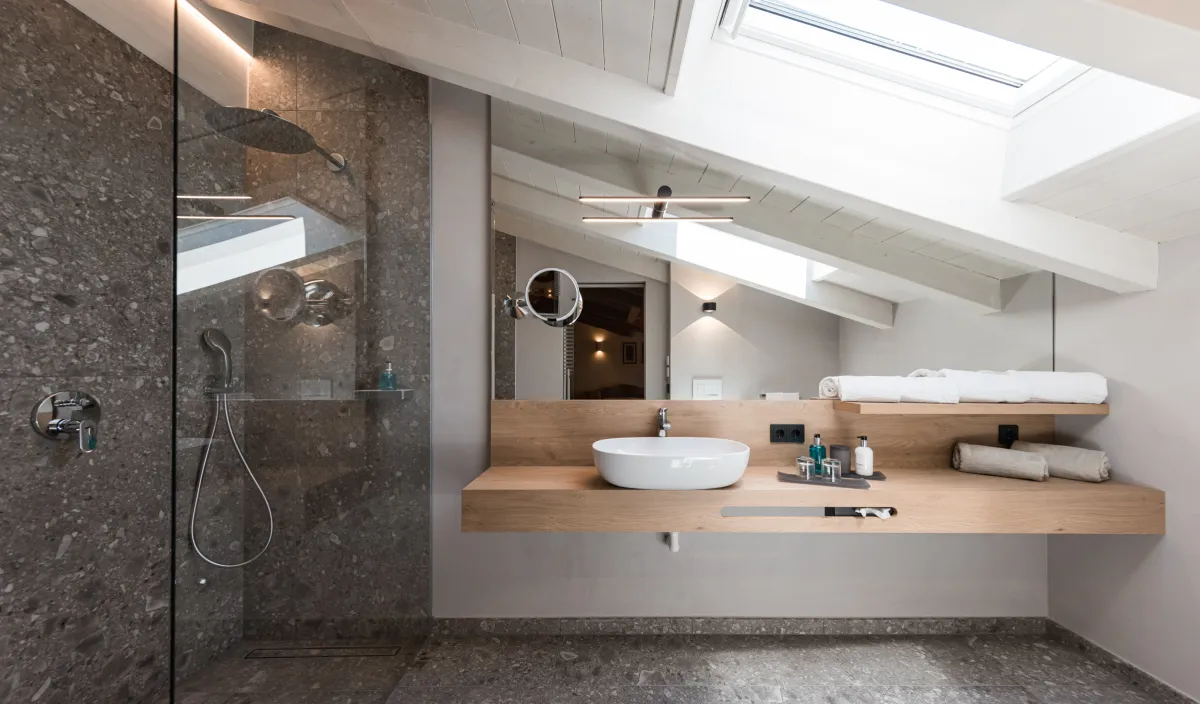 Badezimmer unter der Dachschräge mit begehbarer Dusche, Holzwaschtisch mit Aufsatzwaschbecken und Dachfenster.