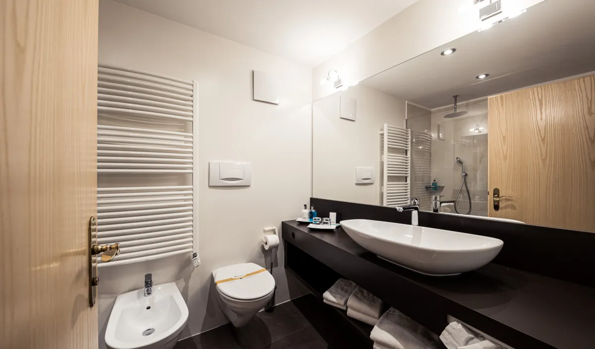 Badezimmer mit dunklem Waschtisch, grossem Waschbecken, Spiegel, WC, Bidet und Handtuchheizkörper.