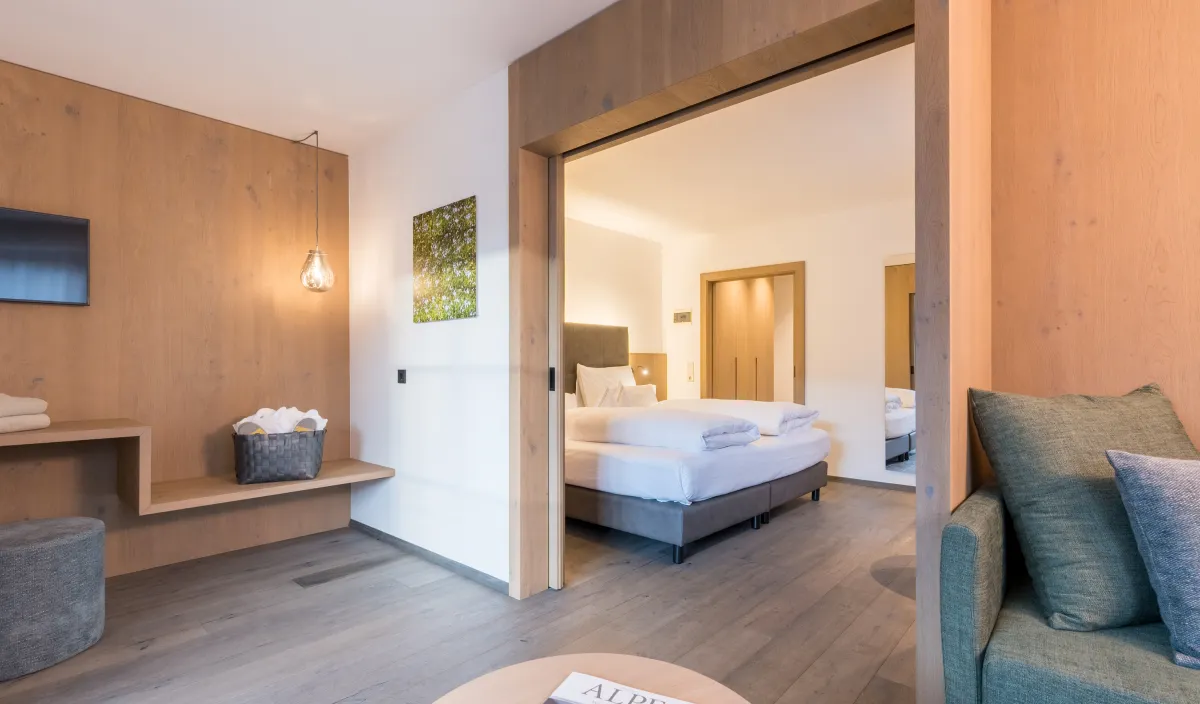Zona giorno con divano verde, tavolino, televisore e passaggio alla camera da letto della Sun Suite.