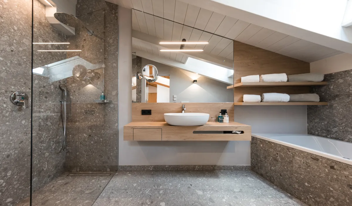 Bagno con doccia walk-in, mobile in legno con lavabo d'appoggio e vasca da bagno sotto il tetto spiovente.