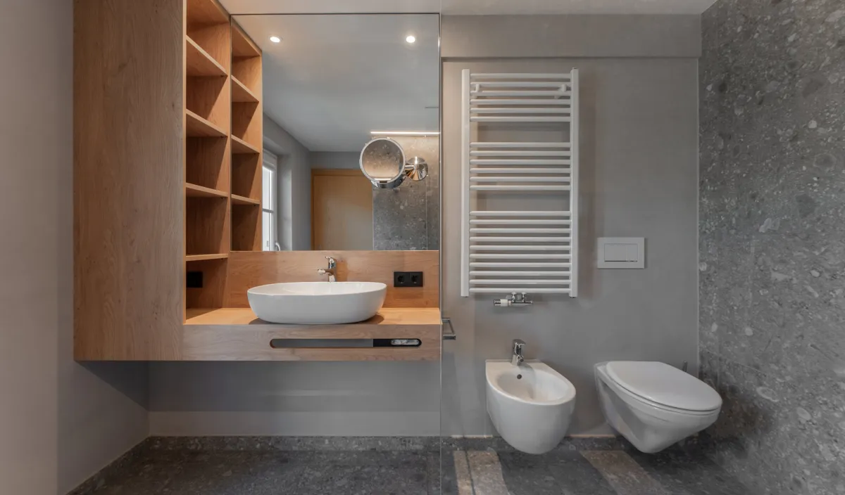 Badezimmer mit Aufsatzwaschbecken auf Holzwaschtisch, offenen Holzregalen, Bidet, WC und Handtuchheizkörper.