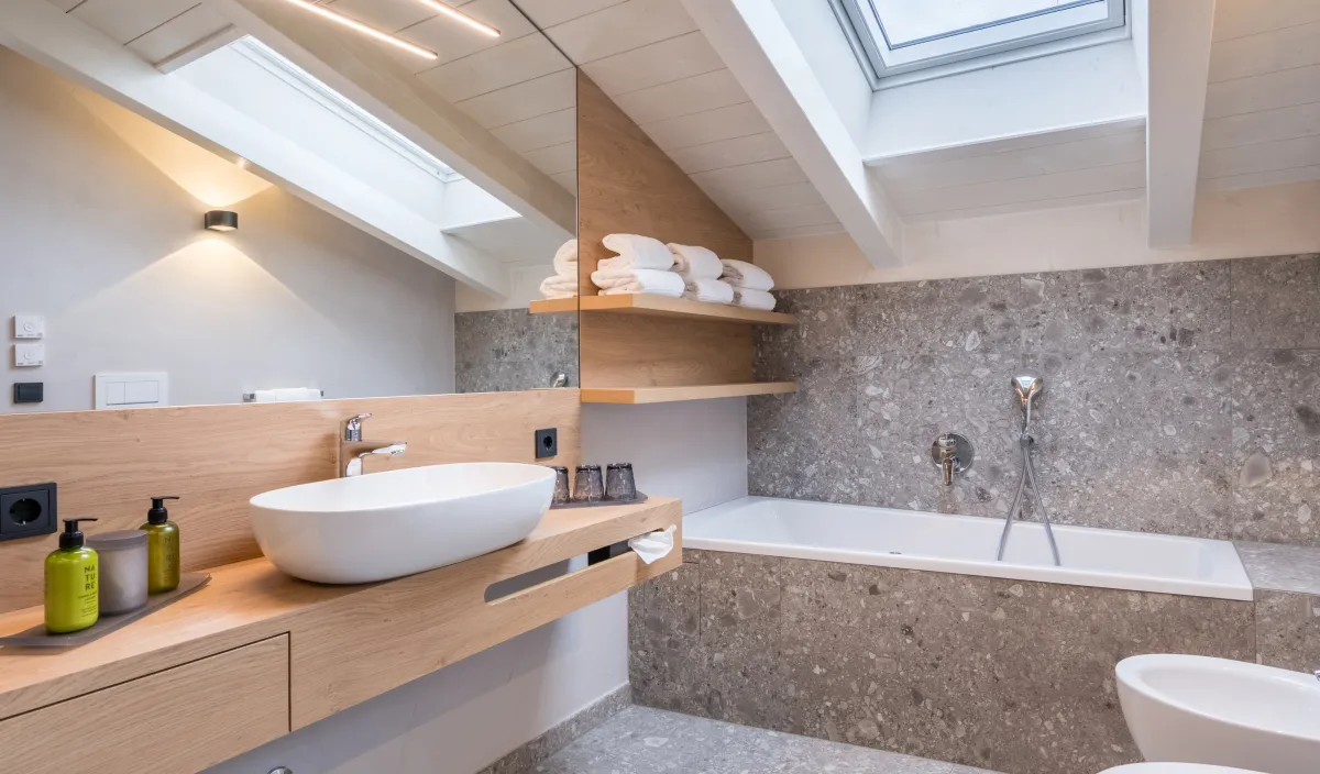 Dettaglio del bagno con lavabo, vasca da bagno, piastrelle in terrazzo di pietra naturale e lucernario con vista sul cielo.