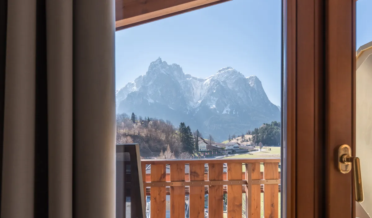 Vista dal balcone sulle montagne con ringhiera in legno e tenda in primo piano.