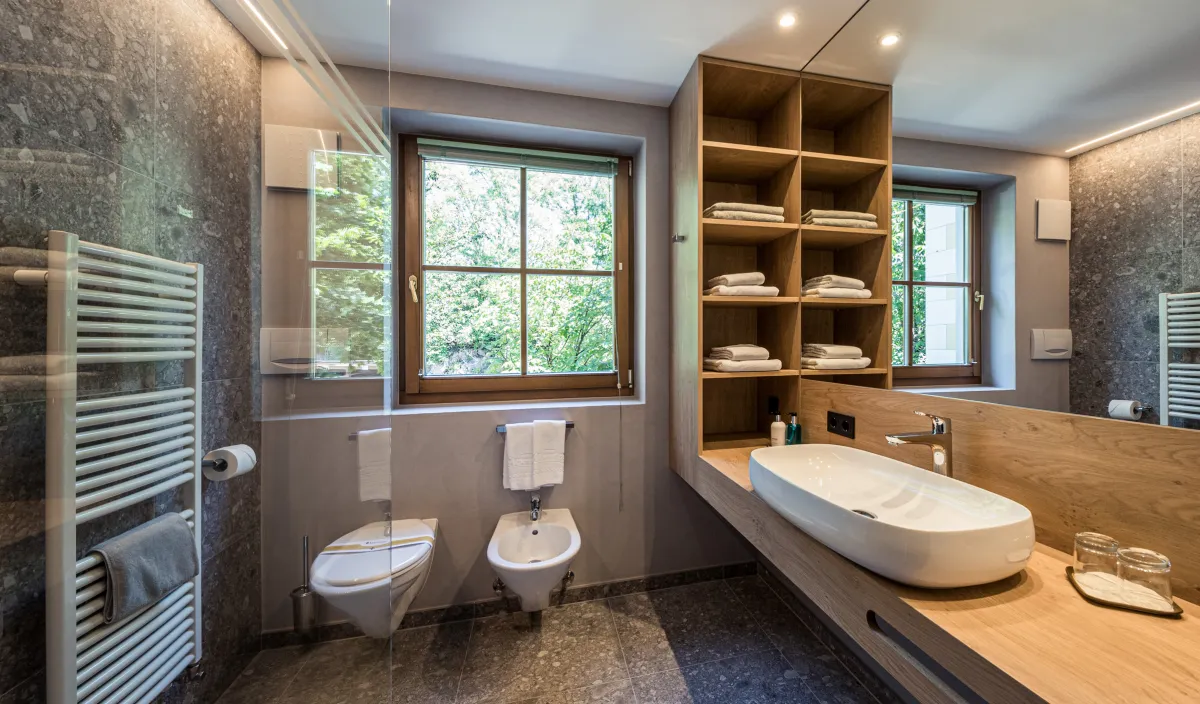Ampio bagno con lavabo, WC, bidet, mensole per asciugamani, finestra e pavimento in pietra naturale.