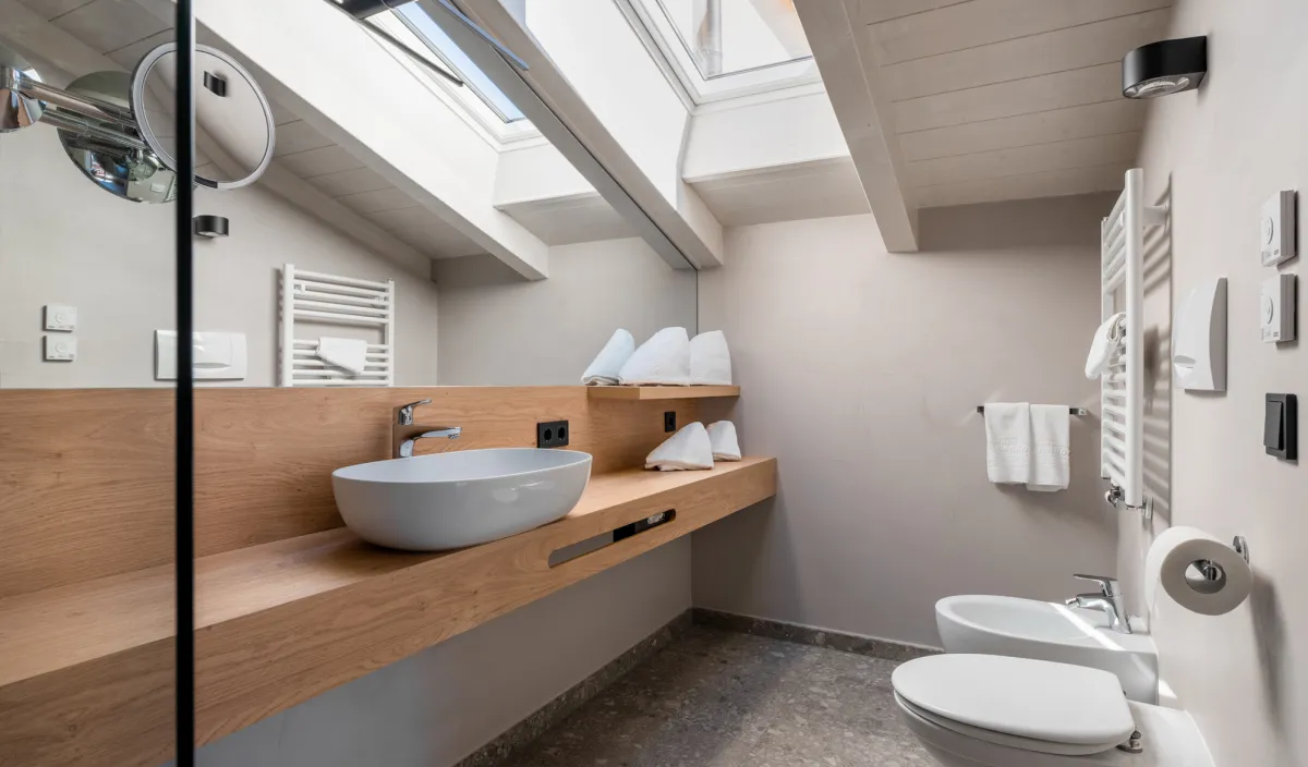 Bagno sotto il tetto spiovente con lavabo su piano in legno, bidet, WC e lucernario.