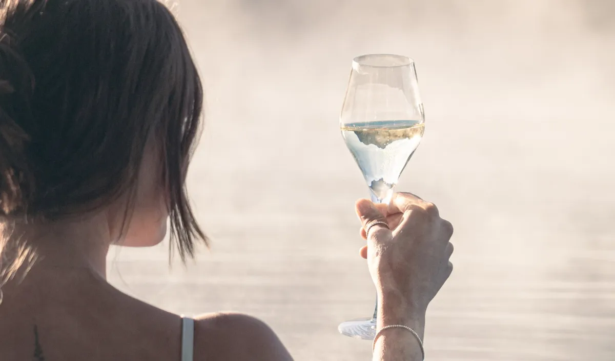 Woman relaxing in the steaming outdoor pool with a glass of white wine in her hand.