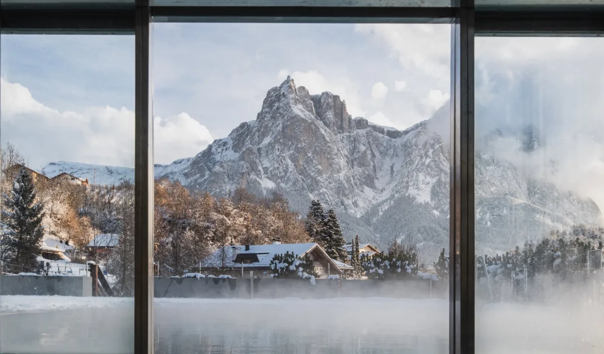 Vista dalla piscina attraverso la vetrata sulla montagna innevata e sull’acqua fumante.