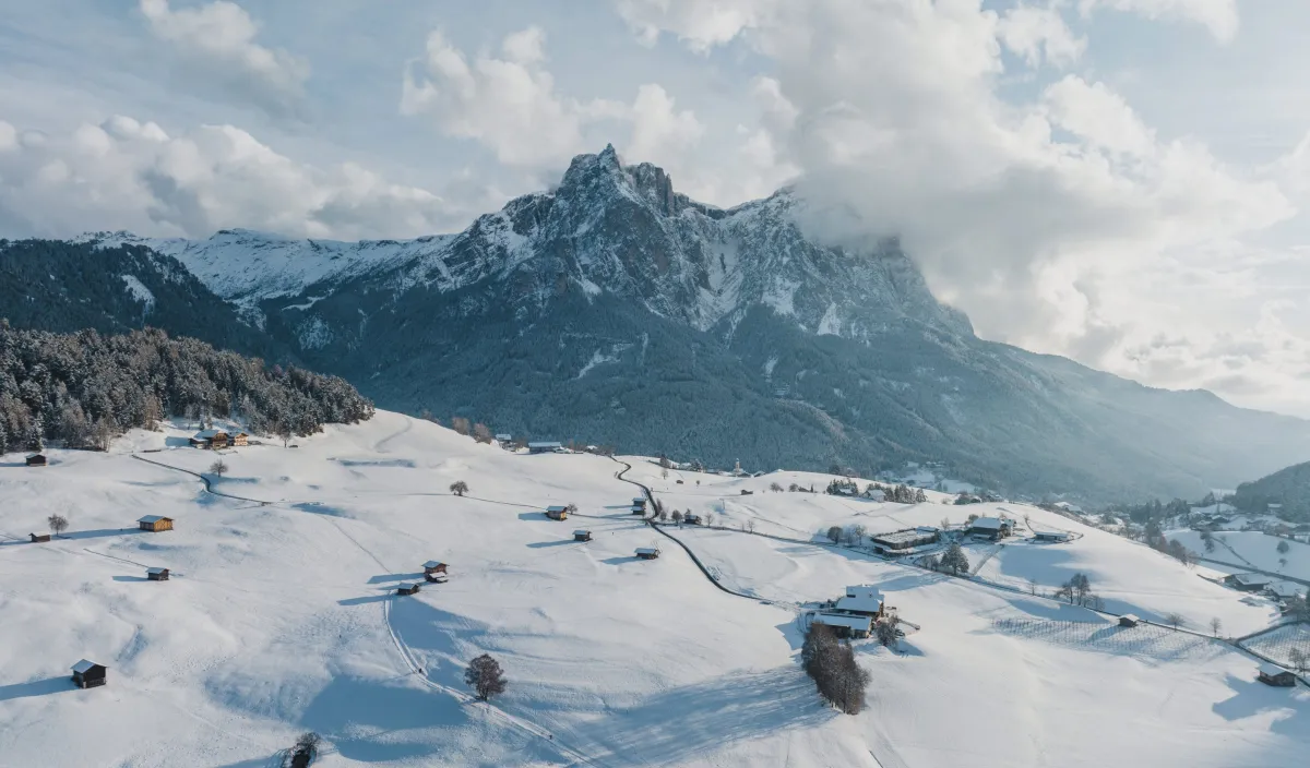 Snow-covered winter landscape near Castelrotto with farmhouses, hay barns and views of the Sciliar.