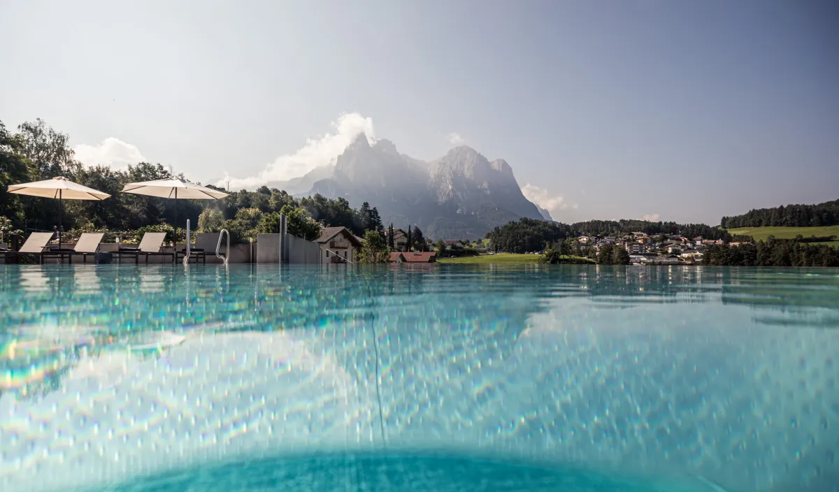 Infinity pool at the Alpenflora with loungers and parasols before the Dolomites of the Alpe di Siusi