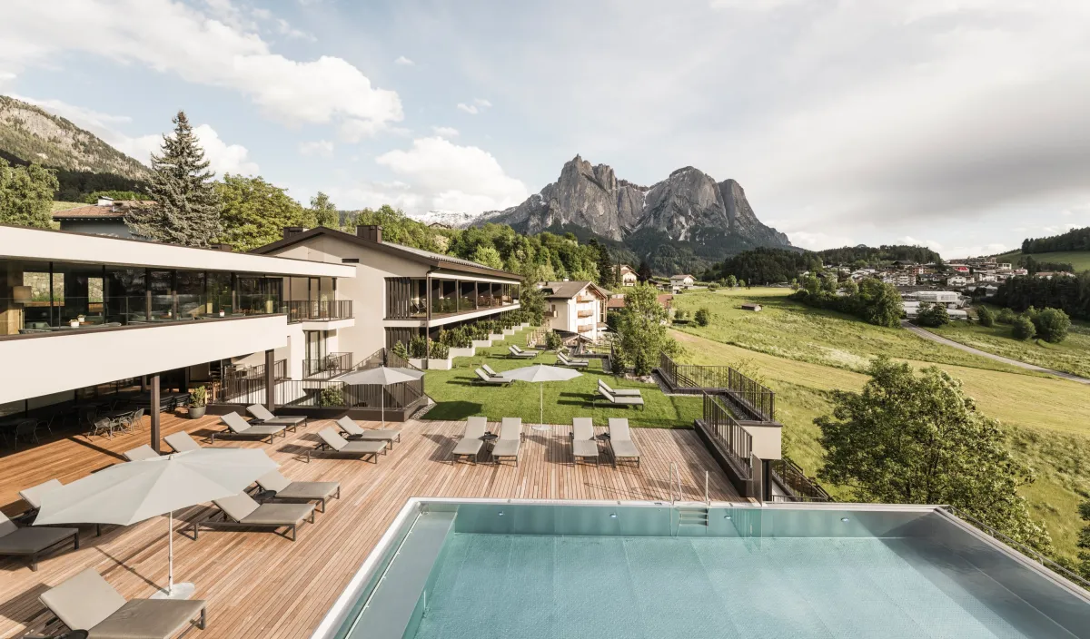 Wellness Hotel Alpenflora in Castelrotto in summer, outdoor pool and terrace amid green meadows and Dolomites