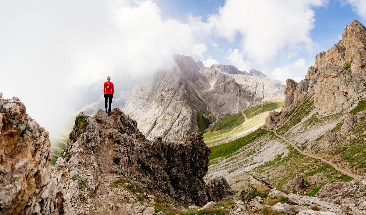 Wanderin in rotem Oberteil auf einem Felsgrat mit Blick auf die Dolomiten nahe dem Wellnesshotel Alpenflora