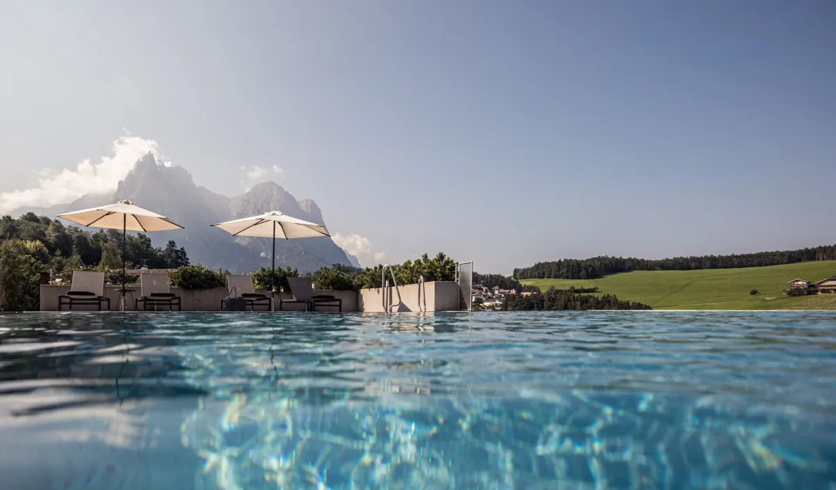 Infinity-Pool des Wellnesshotels Alpenflora mit Blick auf den Schlern und die Sommerwiesen bei Kastelruth.