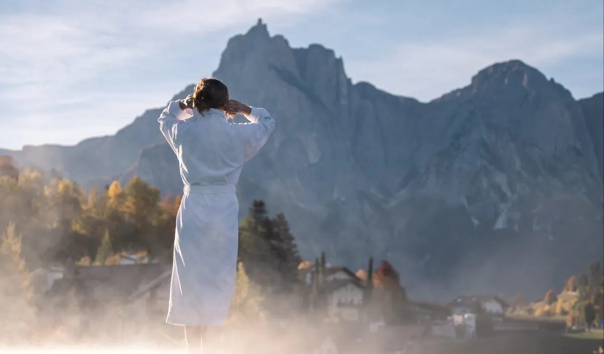 Woman in a bathrobe looking from the Alpenflora terrace at the autumn Dolomites in the morning light