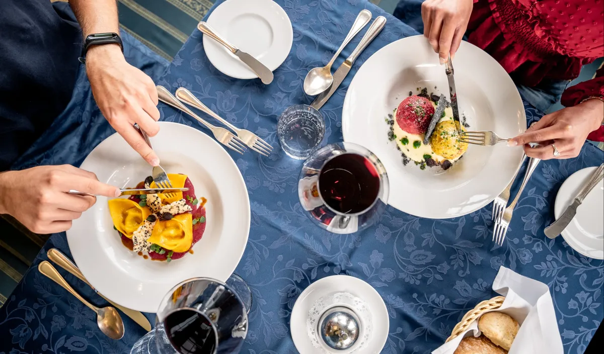 Two guests enjoying South Tyrolean dishes and red wine at a laid table at the Alpenflora