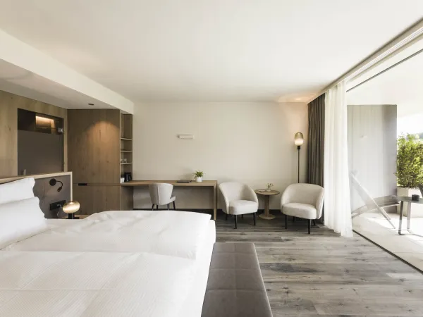Doppelzimmer Garden Relax mit Doppelbett, Schreibtisch, zwei Sesseln und offenem Zugang zur Terrasse.