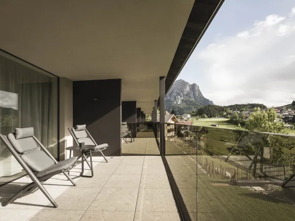 Terrasse des Doppelzimmers Garden View mit Liegestühlen, Glasbalustrade und Blick auf den Schlern.