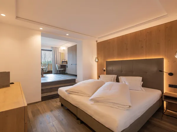 Schlafbereich der Sun Suite im Wellnesshotel Alpenflora mit Doppelbett, Holzwandverkleidung und Durchgang zum Wohnraum.