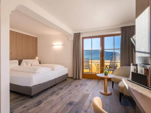 Doppelzimmer Panorama Superior mit Doppelbett, Holzwandverkleidung, Sessel und Balkontür mit Blick ins Grüne.