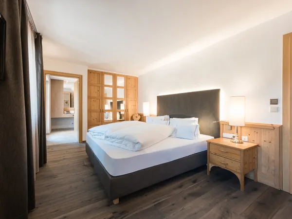 Doppelzimmer Classic mit Doppelbett, Holzschrank mit Glastüren, Nachttischleuchten und Durchgang zum Badezimmer.