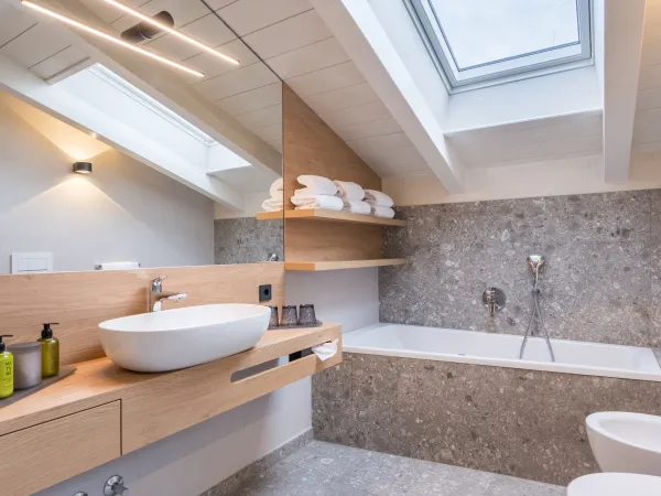 Badezimmer der Attico Suite mit Aufsatzwaschbecken, Badewanne unter der Dachschräge, Dachfenster und Terrazzofliesen.