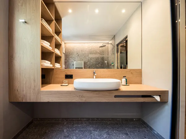 Waschtischbereich der Sun Suite mit Aufsatzwaschbecken, offenem Holzregal mit Handtüchern und Regendusche im Spiegel.