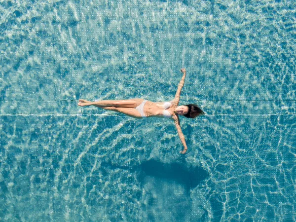 Woman floating relaxed in the clear turquoise water of the pool at the Alpenflora