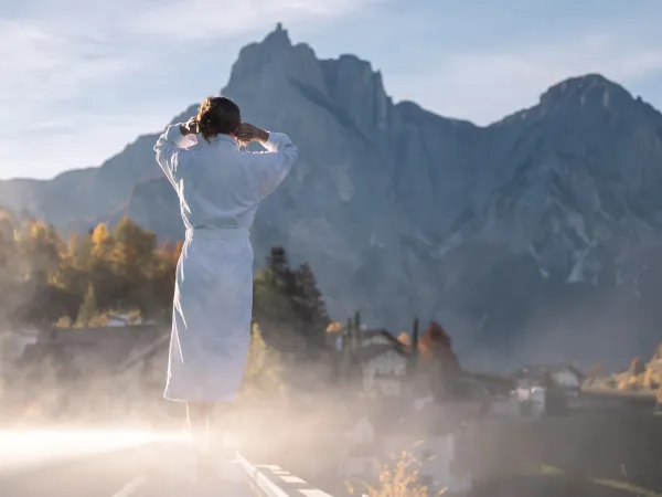 Woman in a bathrobe looking from the Alpenflora terrace at the autumn Dolomites in the morning light