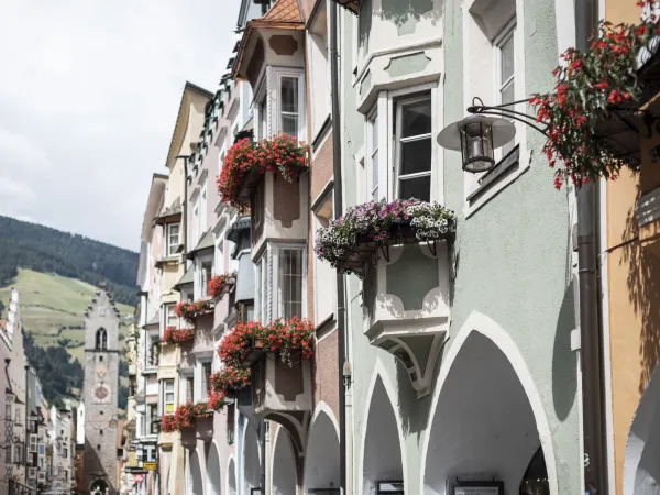 Gasse mit blumengeschmückten Erkerfenstern und einem Stadtturm in Südtirol