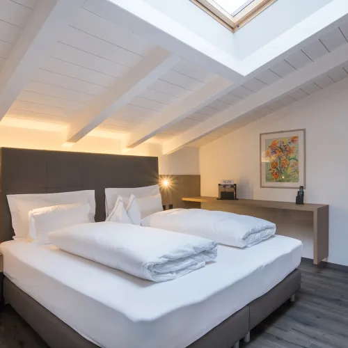 Sleeping area of the Attico Suite with double bed, white beamed ceiling, skylight and floral painting.