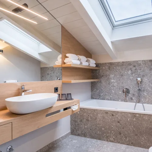 Bathroom of the Attico Suite with vessel sink, bathtub under the sloped ceiling, skylight and terrazzo tiles.
