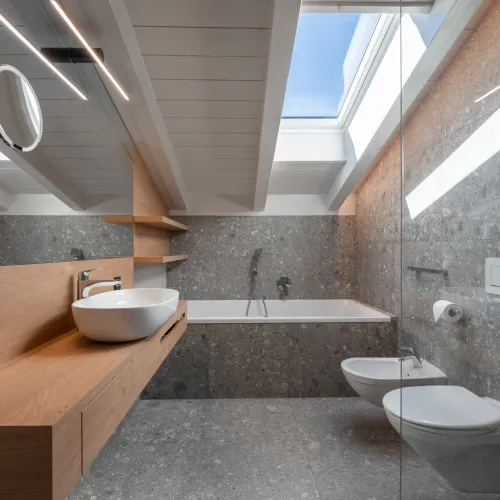 Badezimmer mit Aufsatzwaschbecken auf Holzwaschtisch, Badewanne, Bidet, WC und Dachfenster mit blauem Himmel.