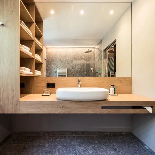 Vanity area of the Sun Suite with vessel sink, open wooden shelf with towels and rain shower visible in the mirror.